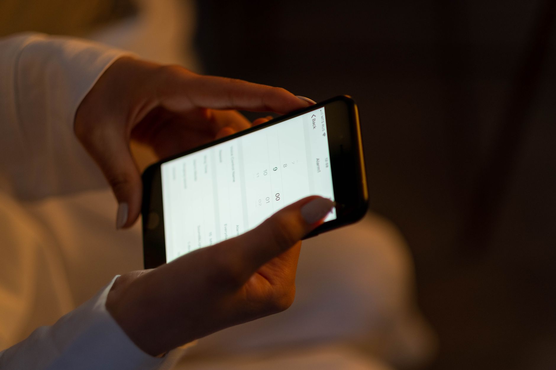 Gros plan sur deux mains qui tiennent un téléphone à l’horizontale dans une pièce tamisée, l’écran éclairé.
